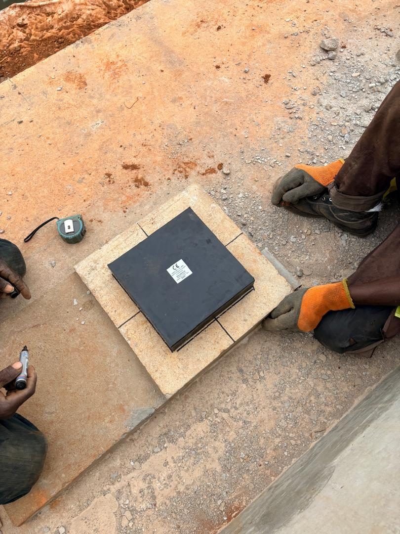 Mains gantées ajustant une plaque noire carrée posée sur une surface en béton, au-dessus d'un gabarit en bois.